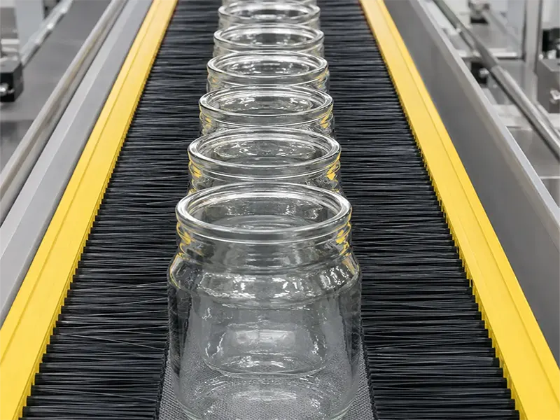 Strip guide brushes positioning glass containers on a beverage conveyor