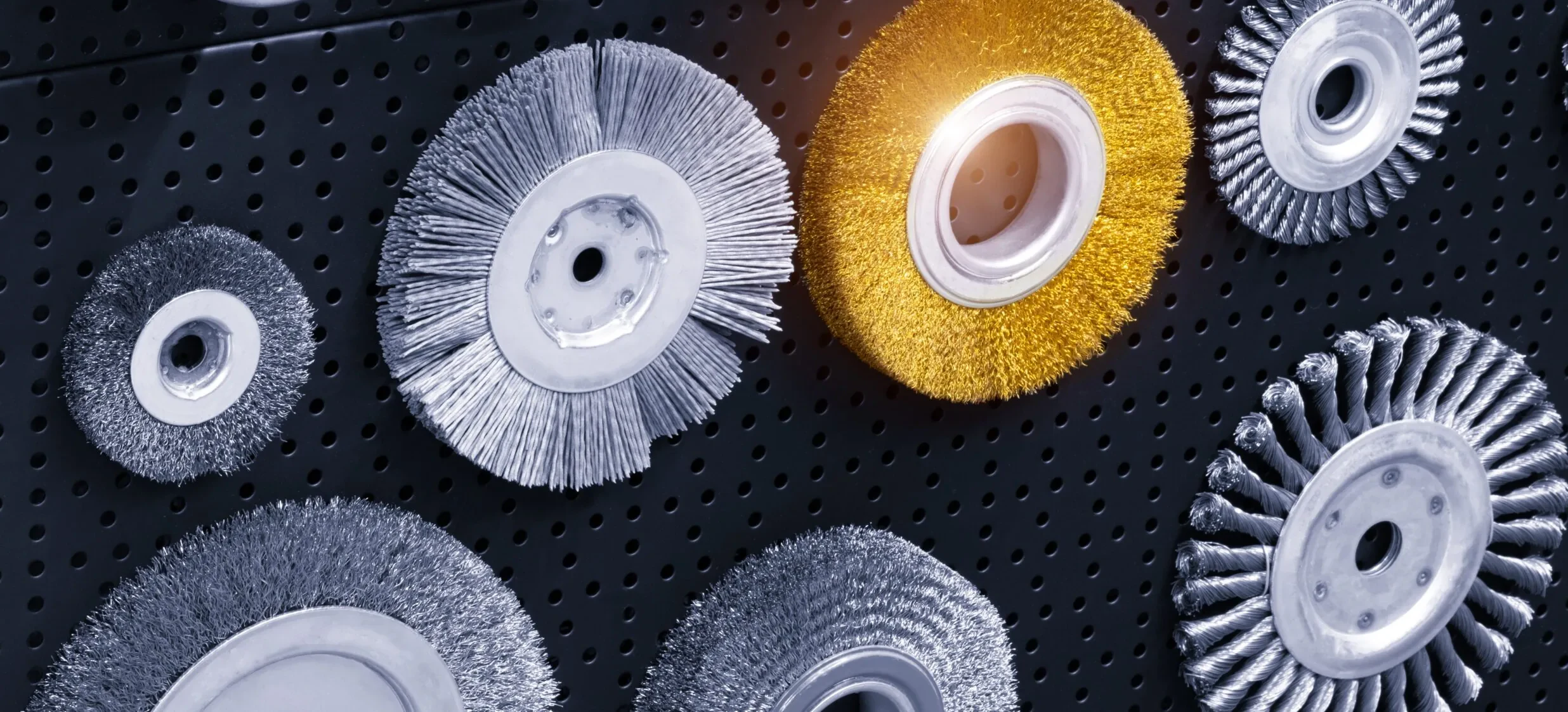 Crimped, brass-coated, and knotted industrial wire wheel brushes displayed on a workshop wall