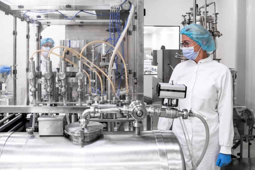 pharmaceutical technician in a protective clothing equipment seen in a laboratory during a manufacturing process